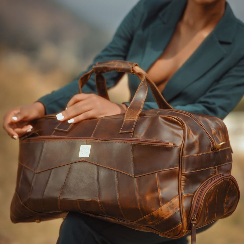 Person holding a brown leather duffel bag with shoe compartent
