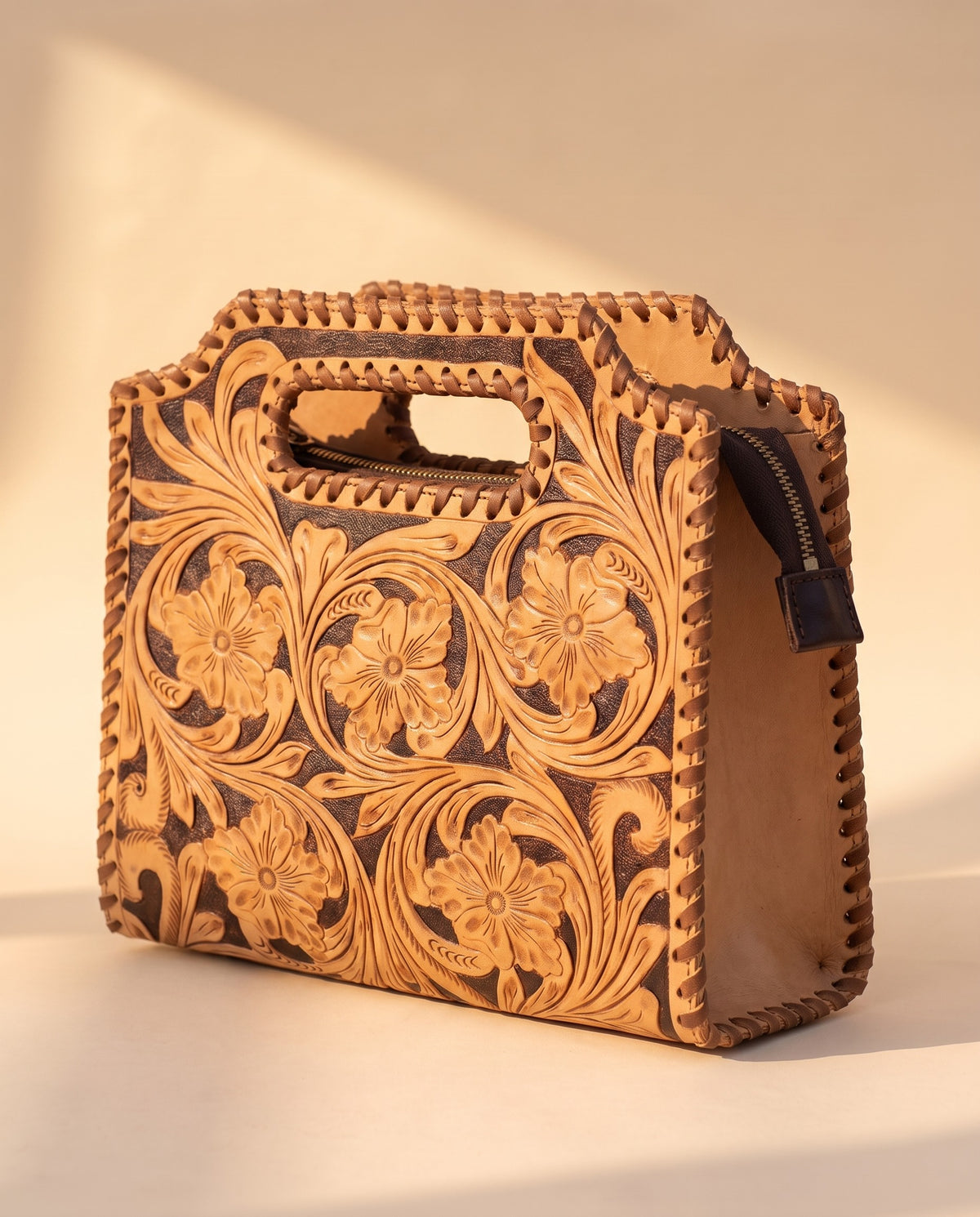 Brown hand-tooled leather bag with cut-out handle, angled view, by Ya Qalbi