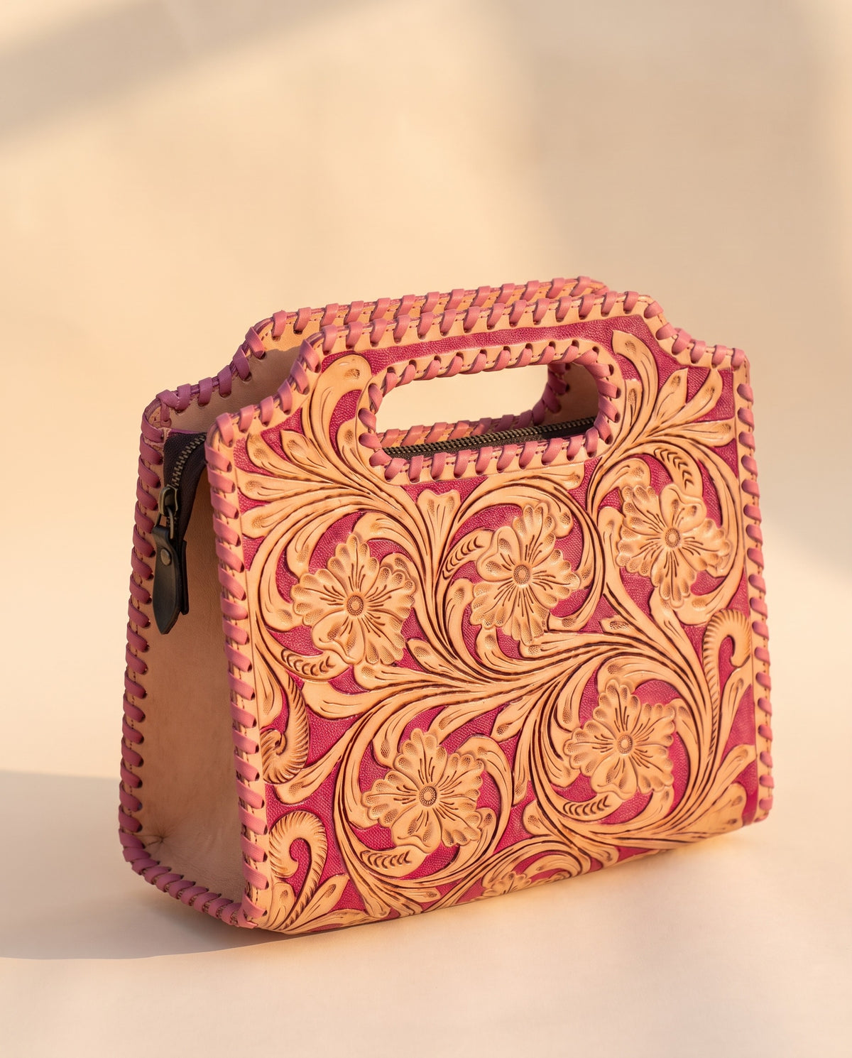 Pink hand-tooled leather bag with cut-out handle, angled view, by Ya Qalbi