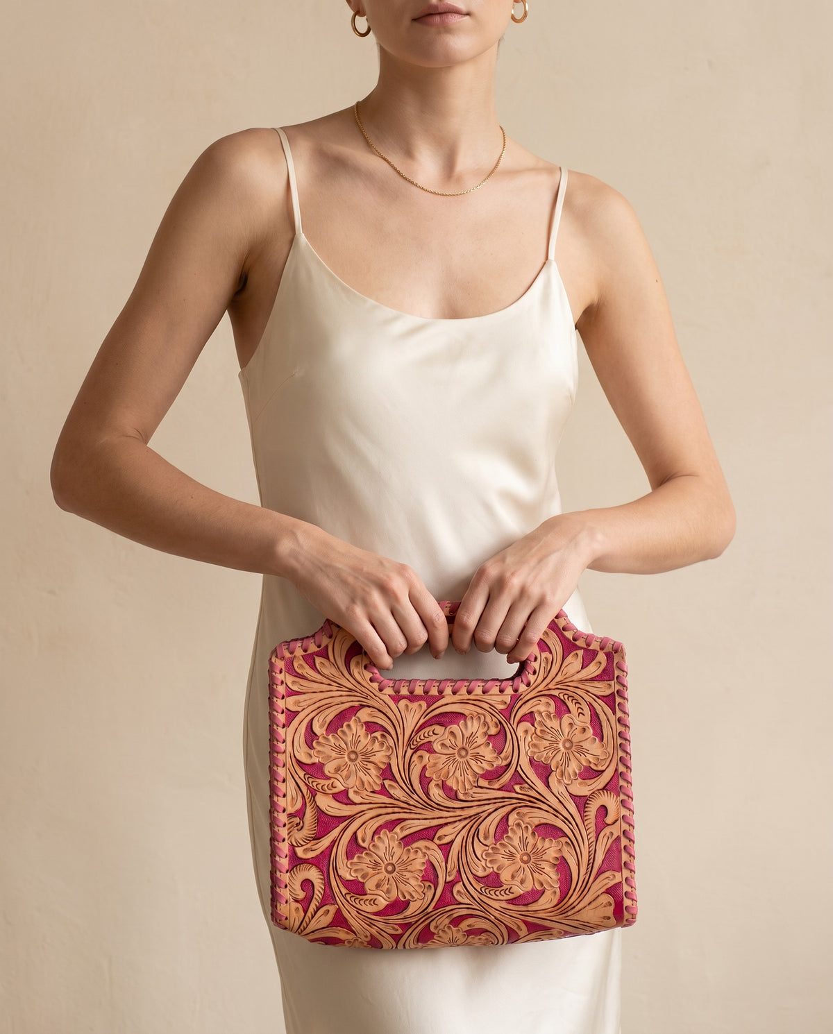 Pink hand-tooled leather bag with cut-out handle, worn by a model, by Ya Qalbi