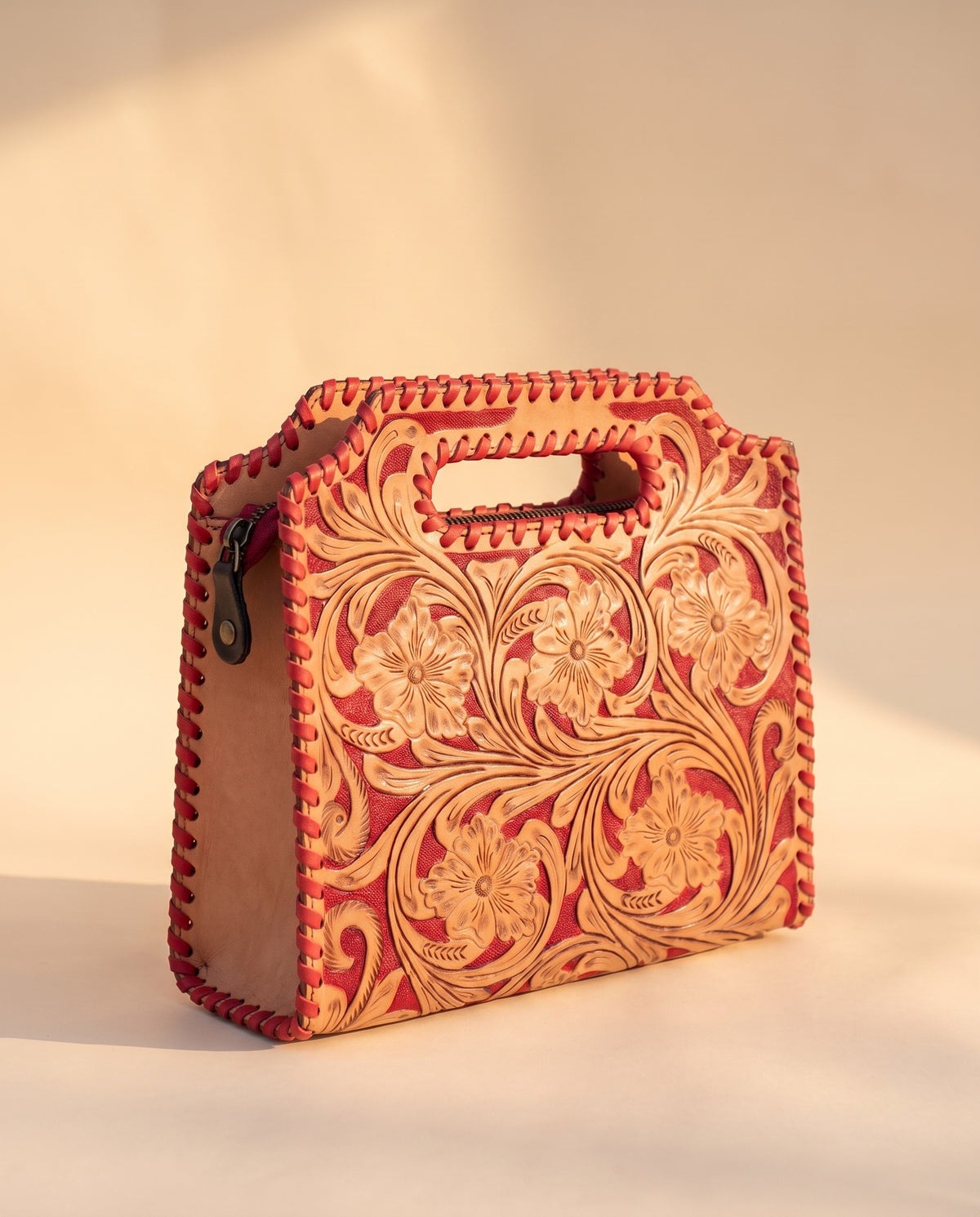Red hand-tooled leather bag with cut-out handle, angled view, by Ya Qalbi