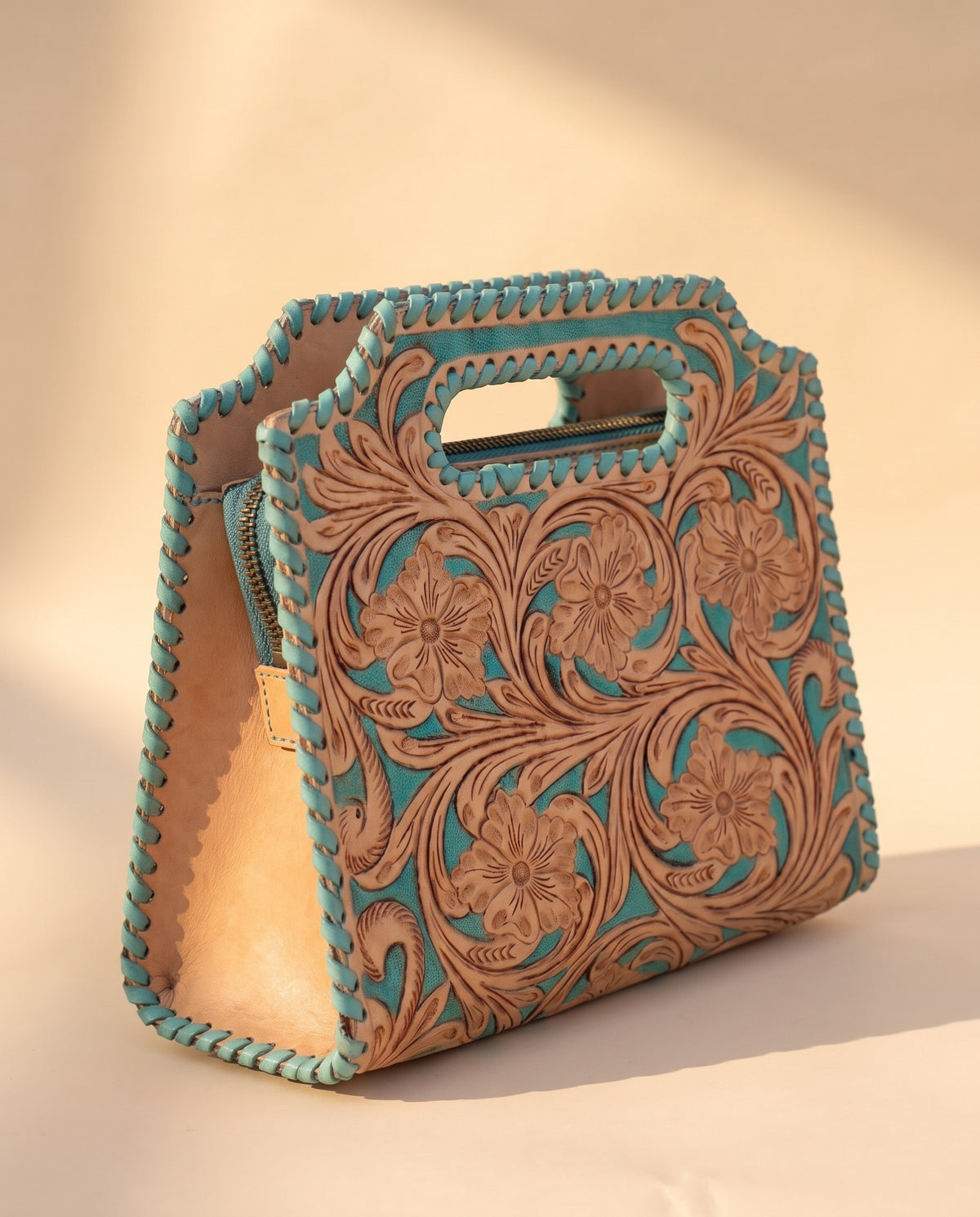 Turquoise hand-tooled leather bag with cut-out handle, angled view, by Ya Qalbi