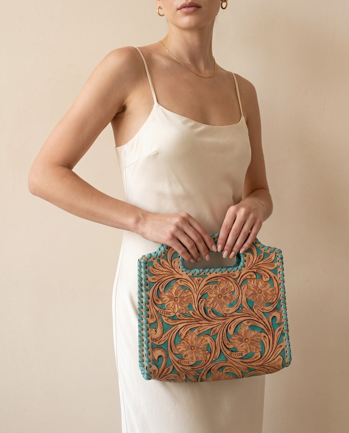 Turquoise hand-tooled leather bag with cut-out handle, worn by a model, by Ya Qalbi