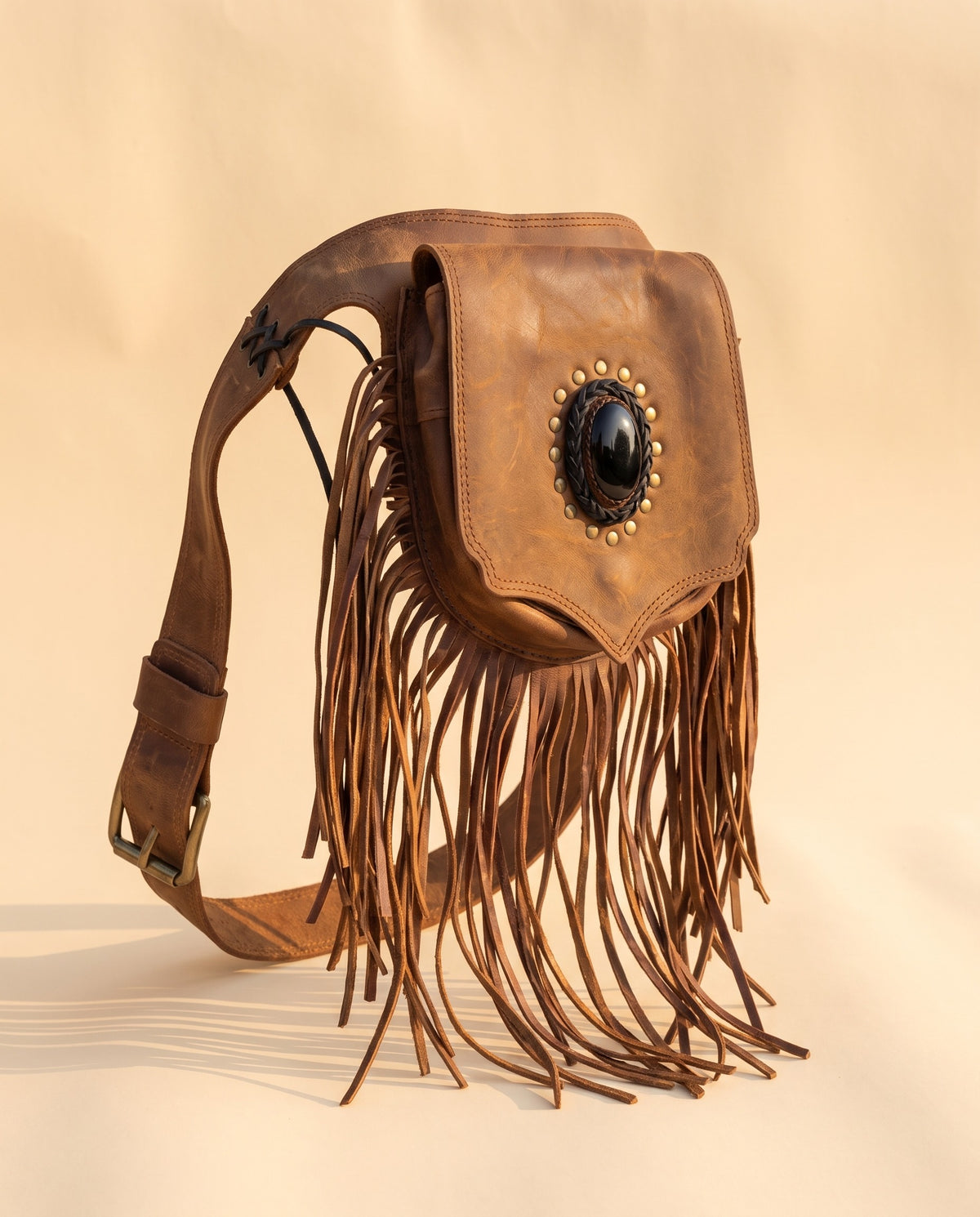 Brown fringe leather hip bag with stone, angled view, by Ya Qalbi