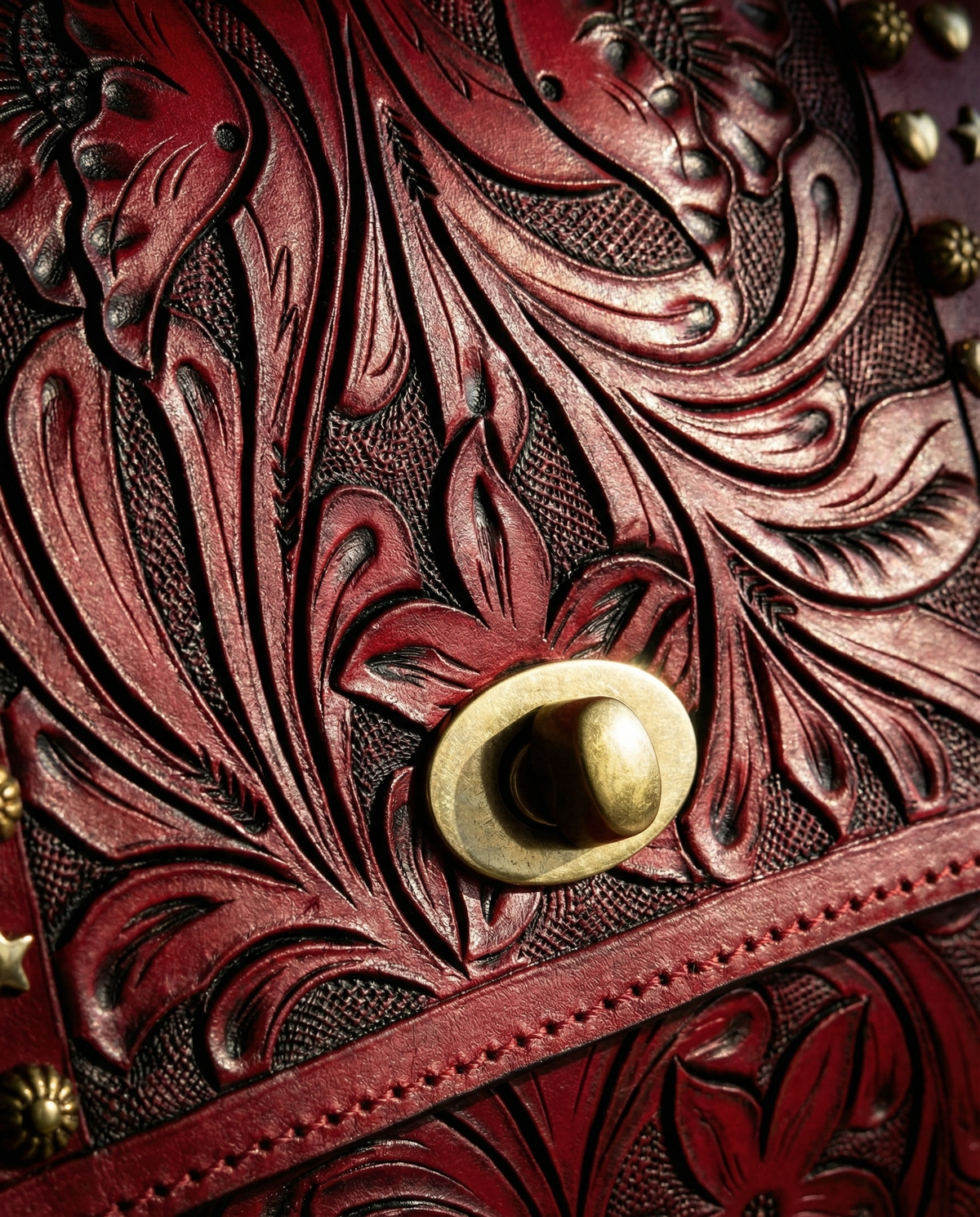 Close-up of floral carving and brass turn-lock on red leather satchel by Ya Qalbi
