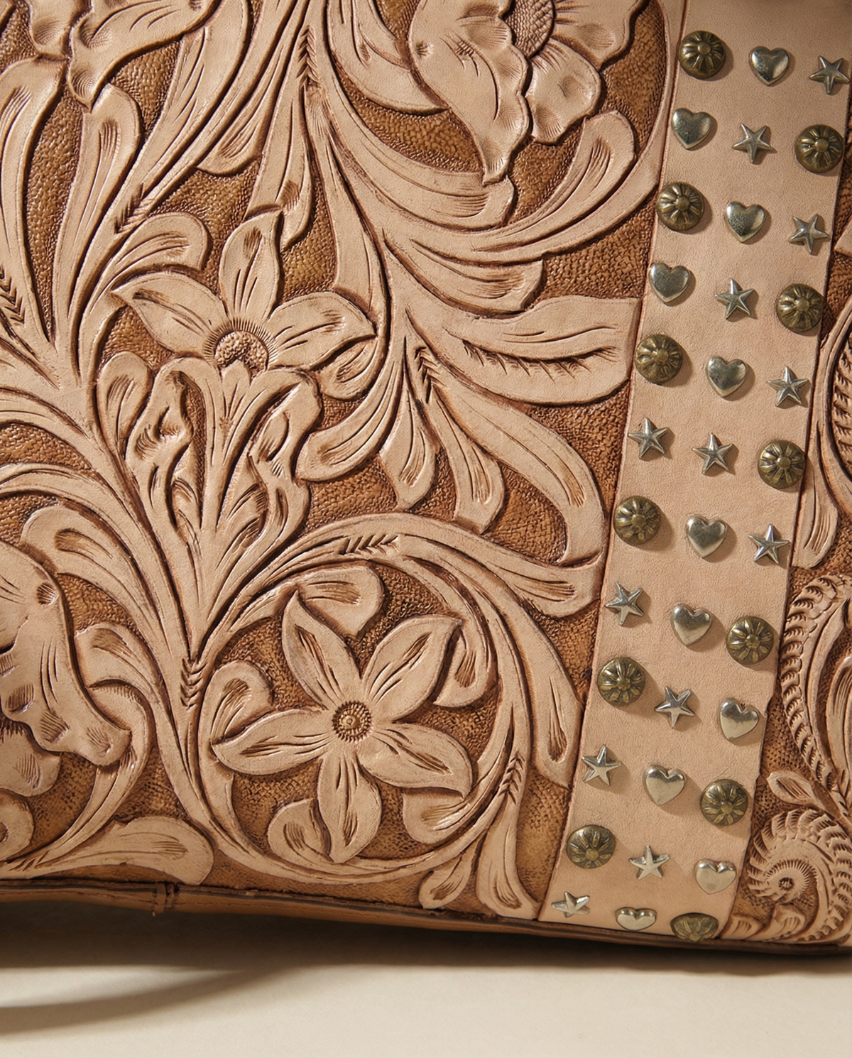 Close-up of floral carving and brass studs on tan tooled leather by Ya Qalbi