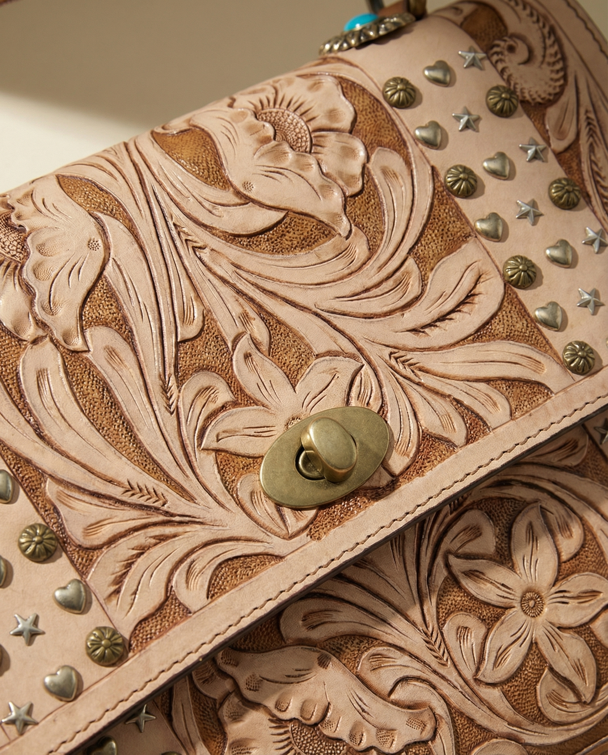Close-up of brass turn-lock on tan tooled leather satchel by Ya Qalbi