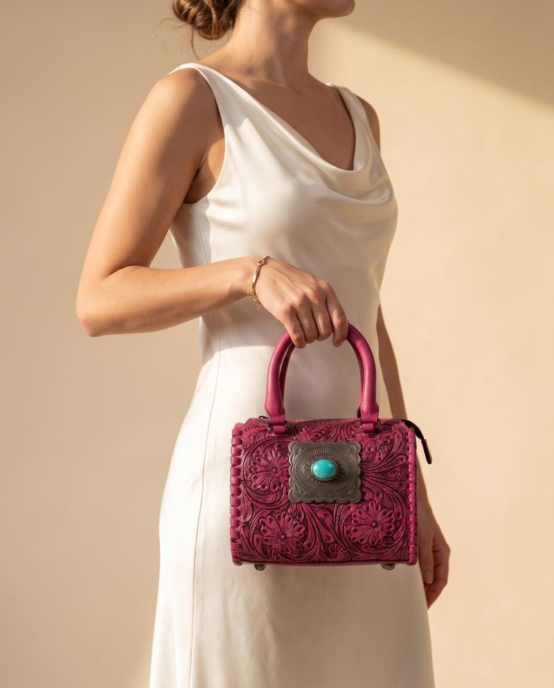 Magenta hand-tooled leather barrel bag with concho, worn by a model, by Ya Qalbi