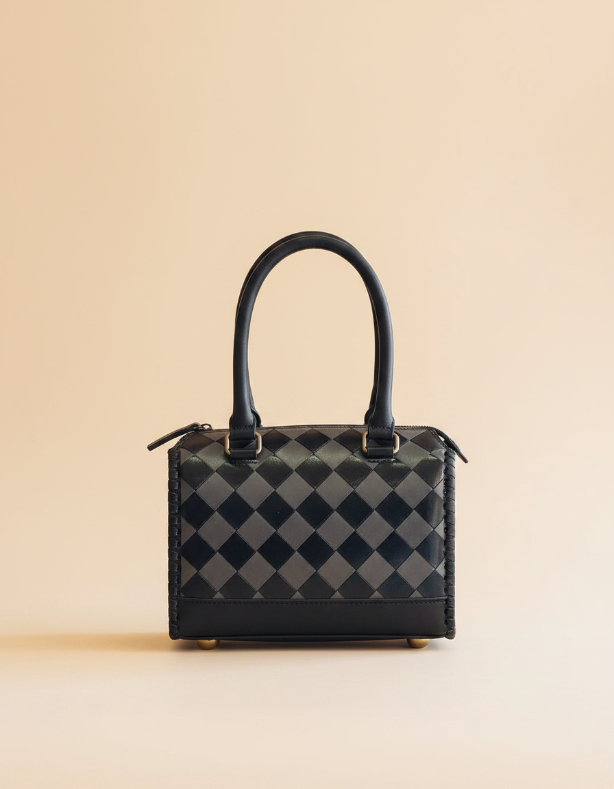 Black and grey checkerboard leather barrel bag with cowhide corner, angled view, by Ya Qalbi