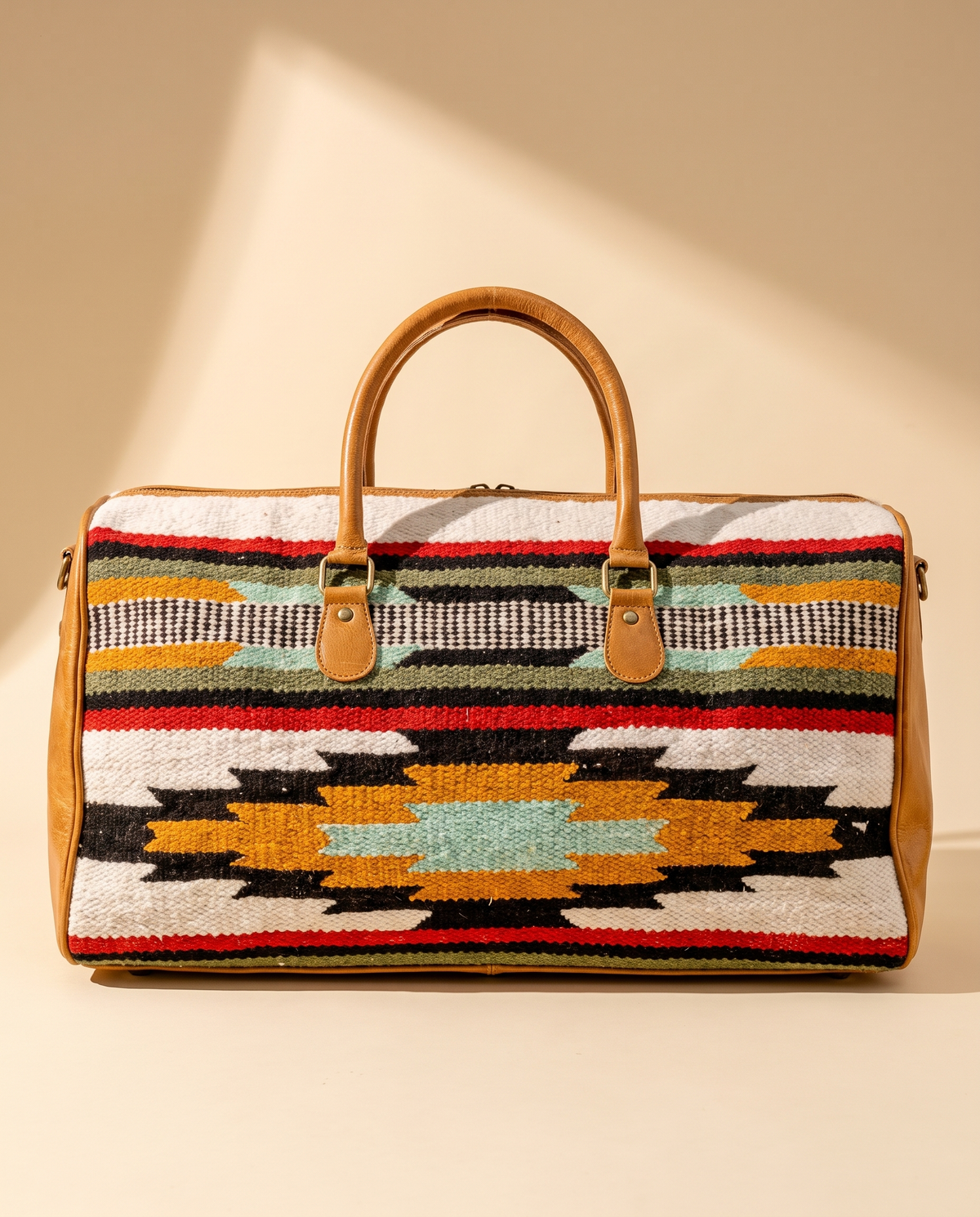 Ivory striped kilim duffle bag with tan leather trim and rolled handles, front view