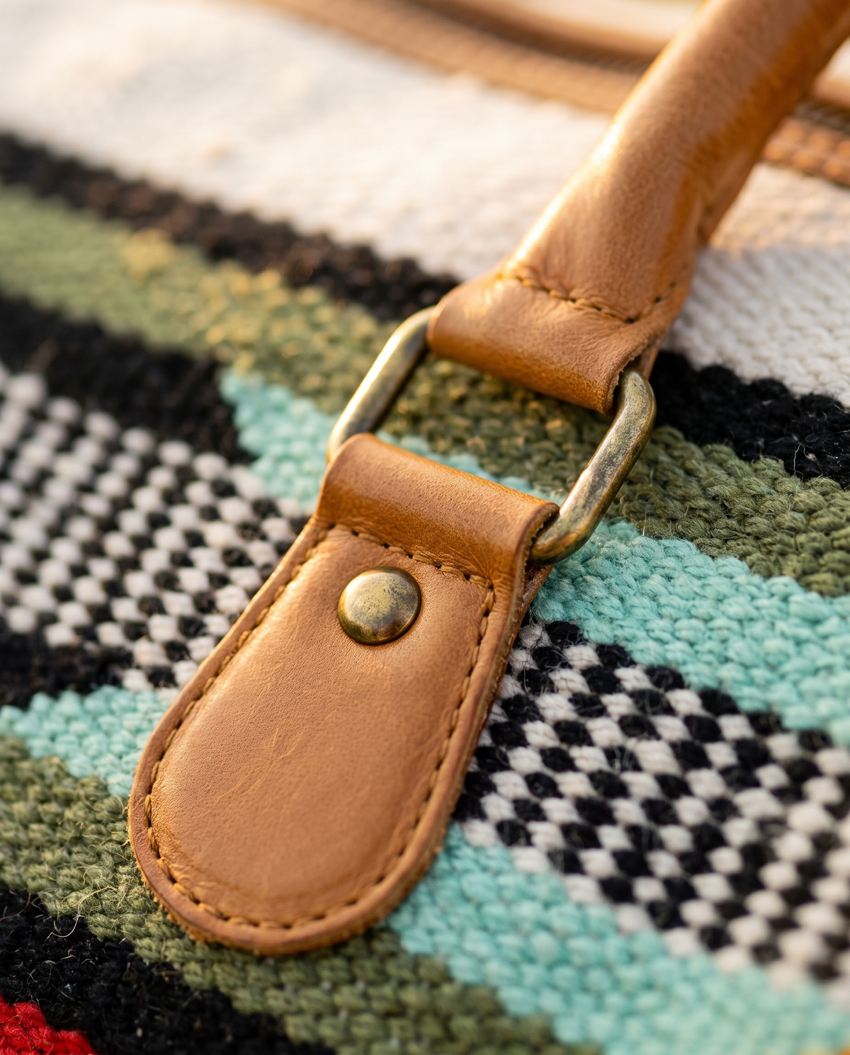 Detail of tan leather handle loop over red, olive and black kilim stripes