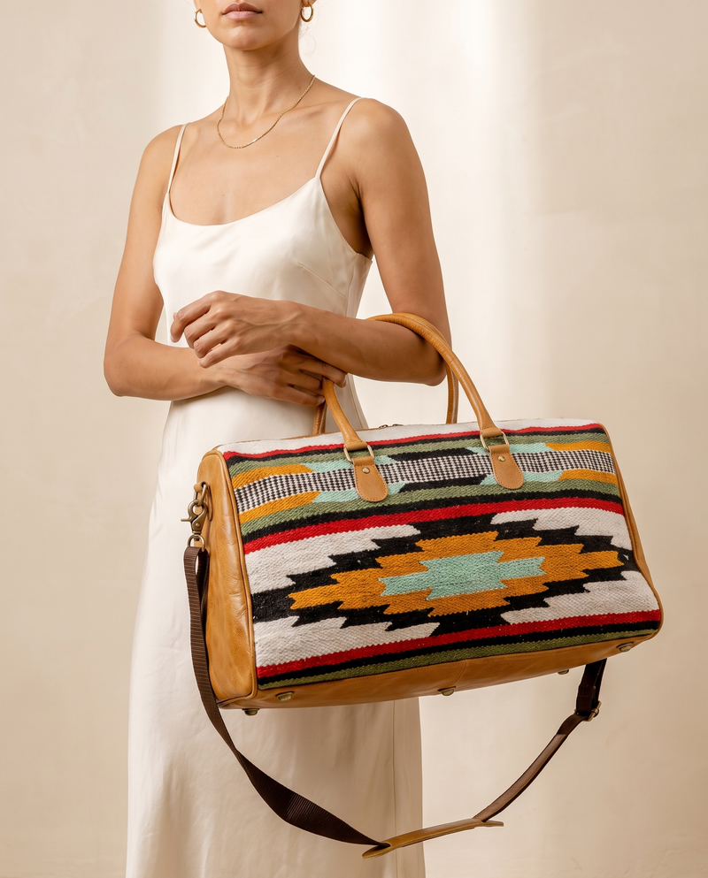 Woman in ivory slip dress holding ivory striped kilim and tan leather duffle bag