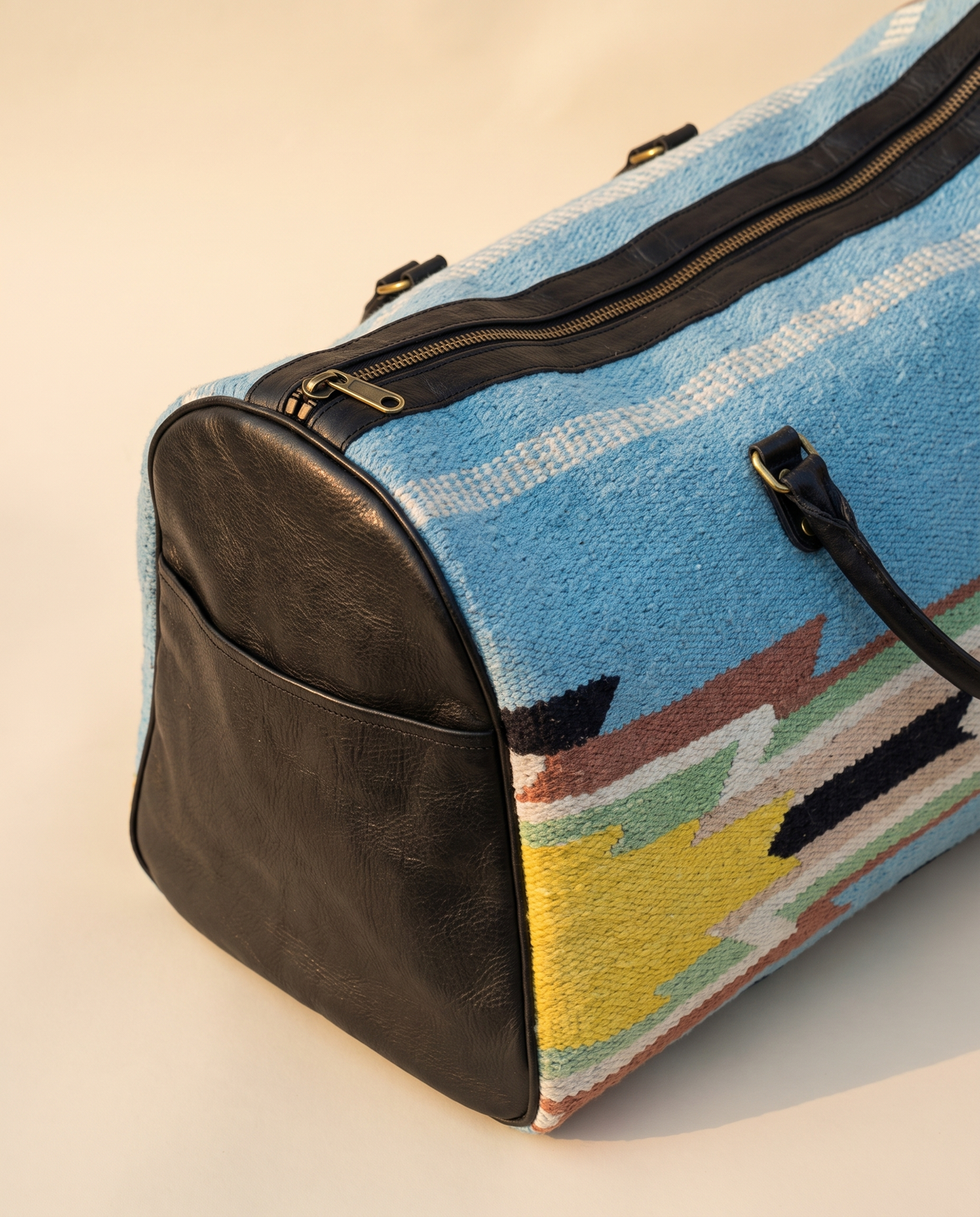 Sky blue kilim weekender showing black leather end panel with outer pocket
