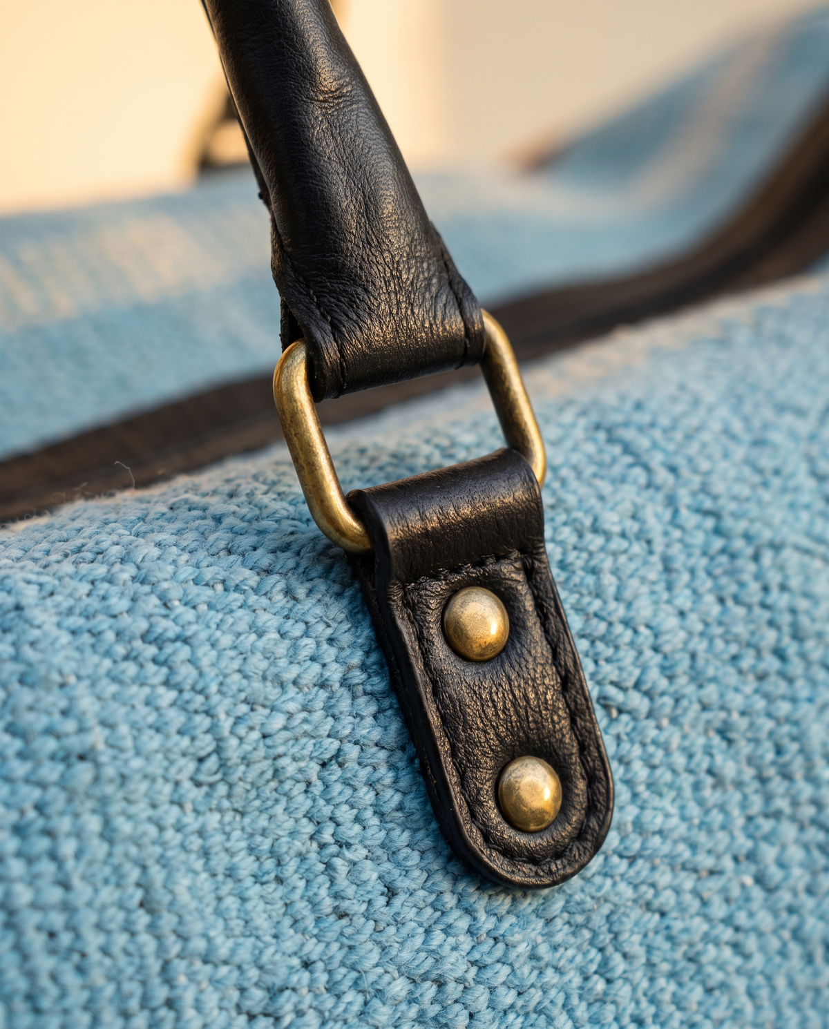 Close-up of black leather handle tab and brass ring on sky blue kilim