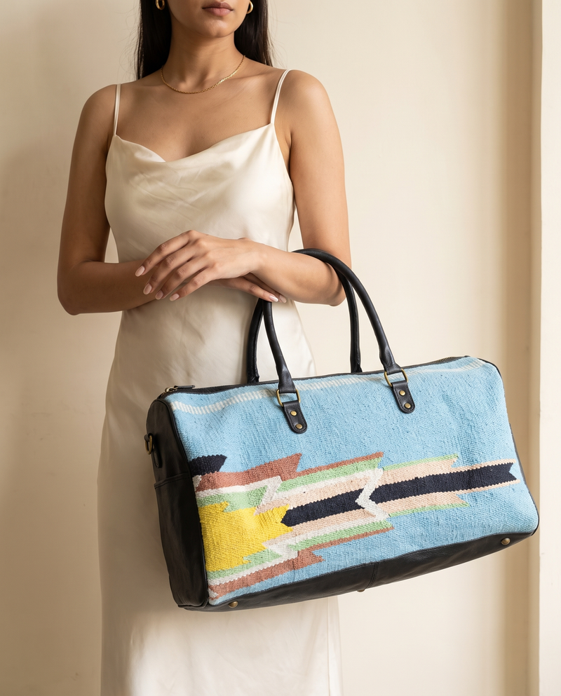 Woman holding sky blue kilim and black leather duffle bag