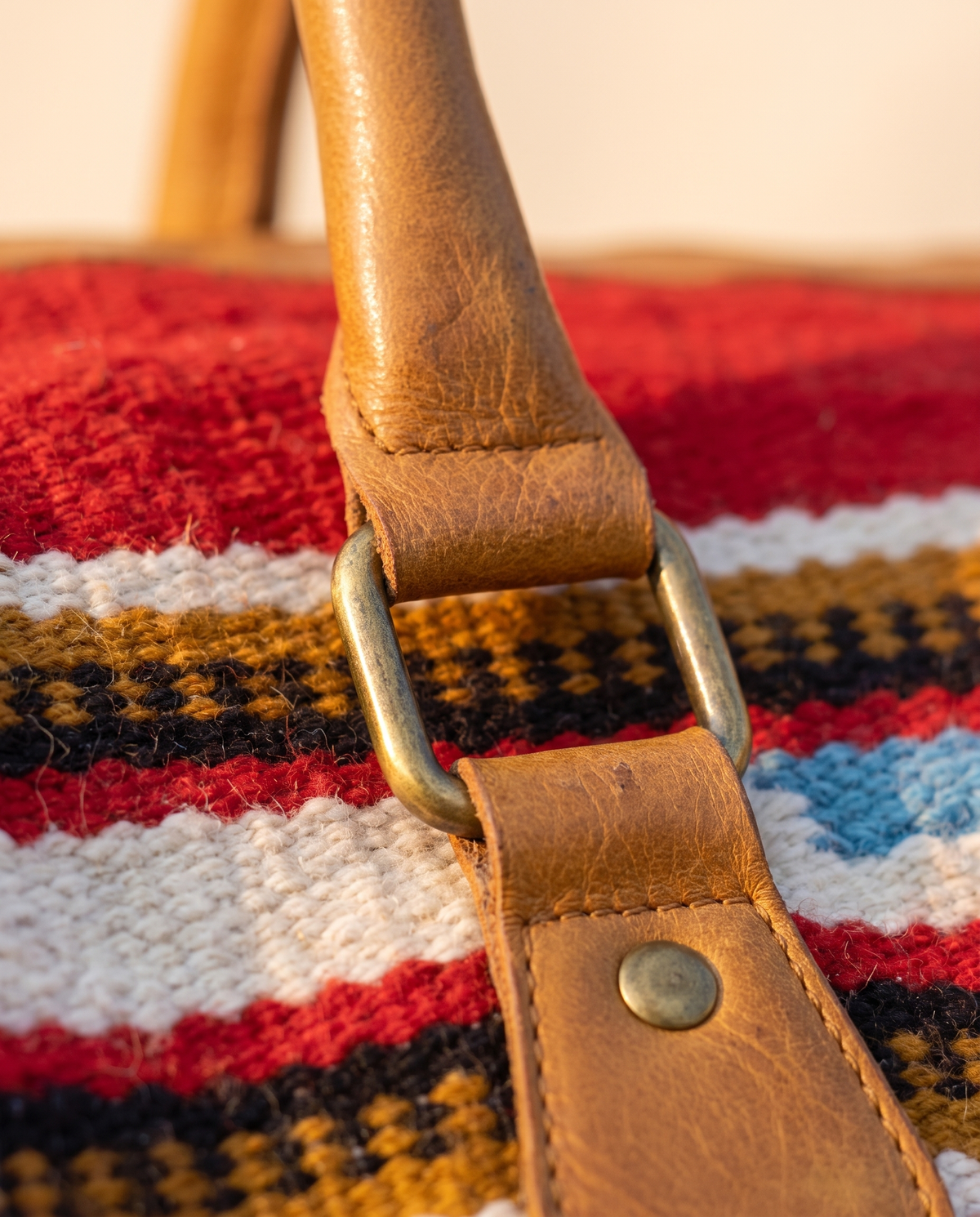Close-up of tan leather handle tab over red and ivory kilim stripes
