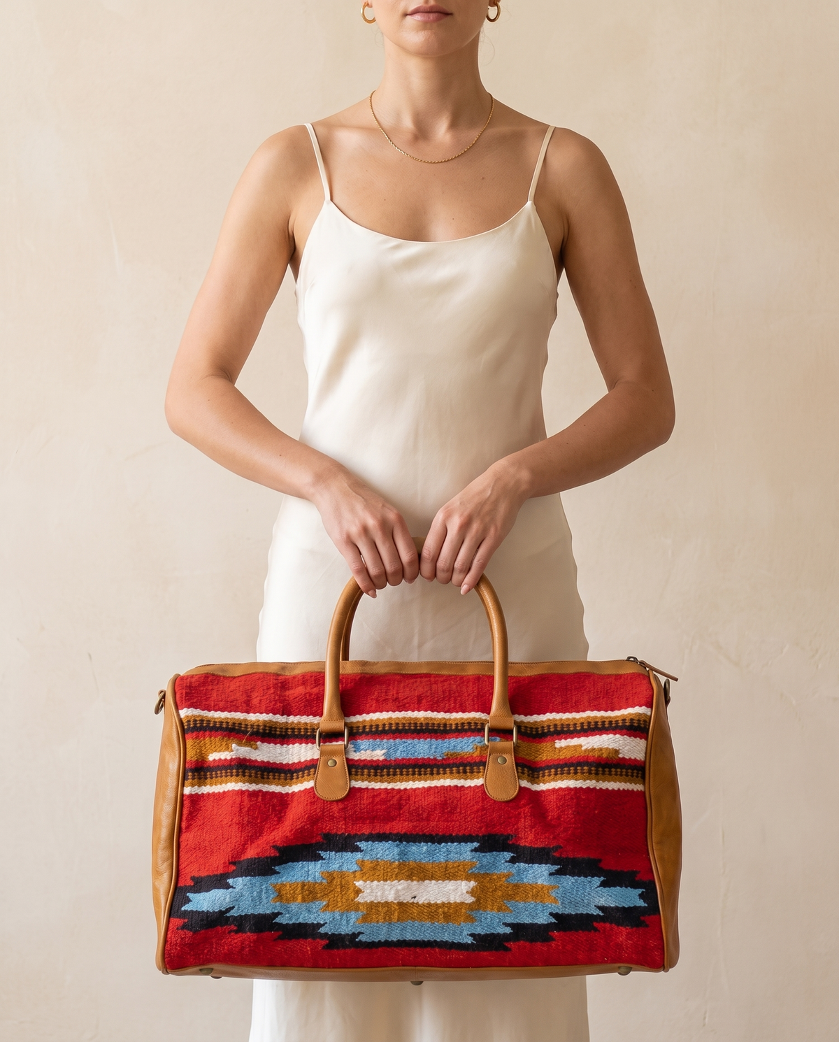 Woman holding red kilim duffle bag with tan leather trim in front of her