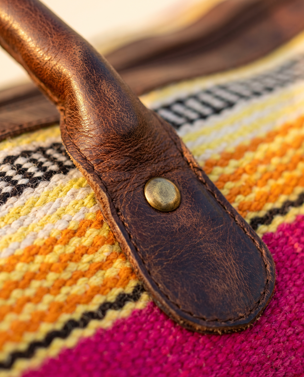 Close-up of dark brown leather handle over yellow and orange kilim stripes