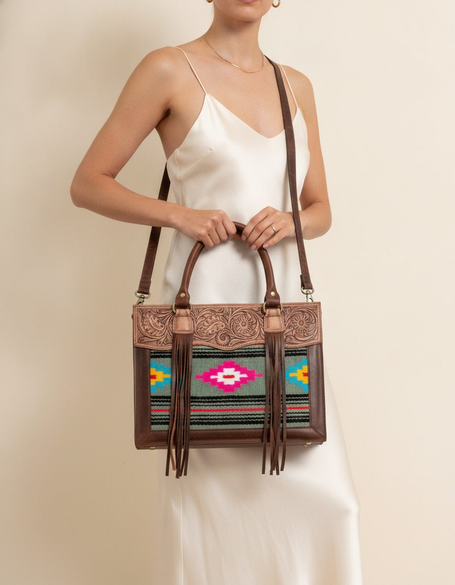 Grey and pink serape fringe tote with tooled leather top, worn by a model, by Ya Qalbi
