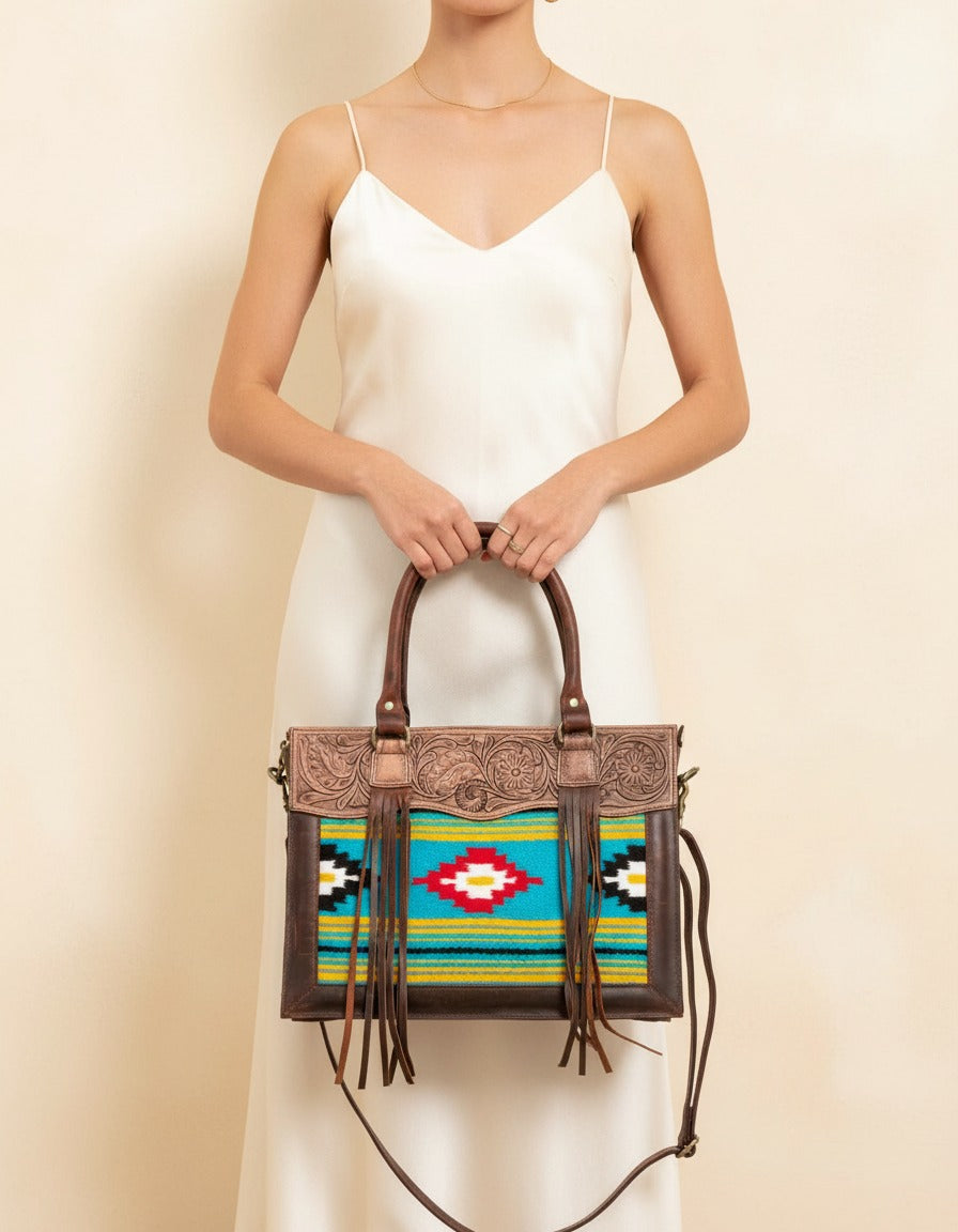 Turquoise and yellow serape fringe tote with tooled leather top, worn by a model, by Ya Qalbi