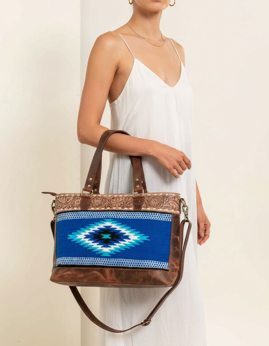 Blue serape woven zip tote with tooled leather band, worn by a model, by Ya Qalbi