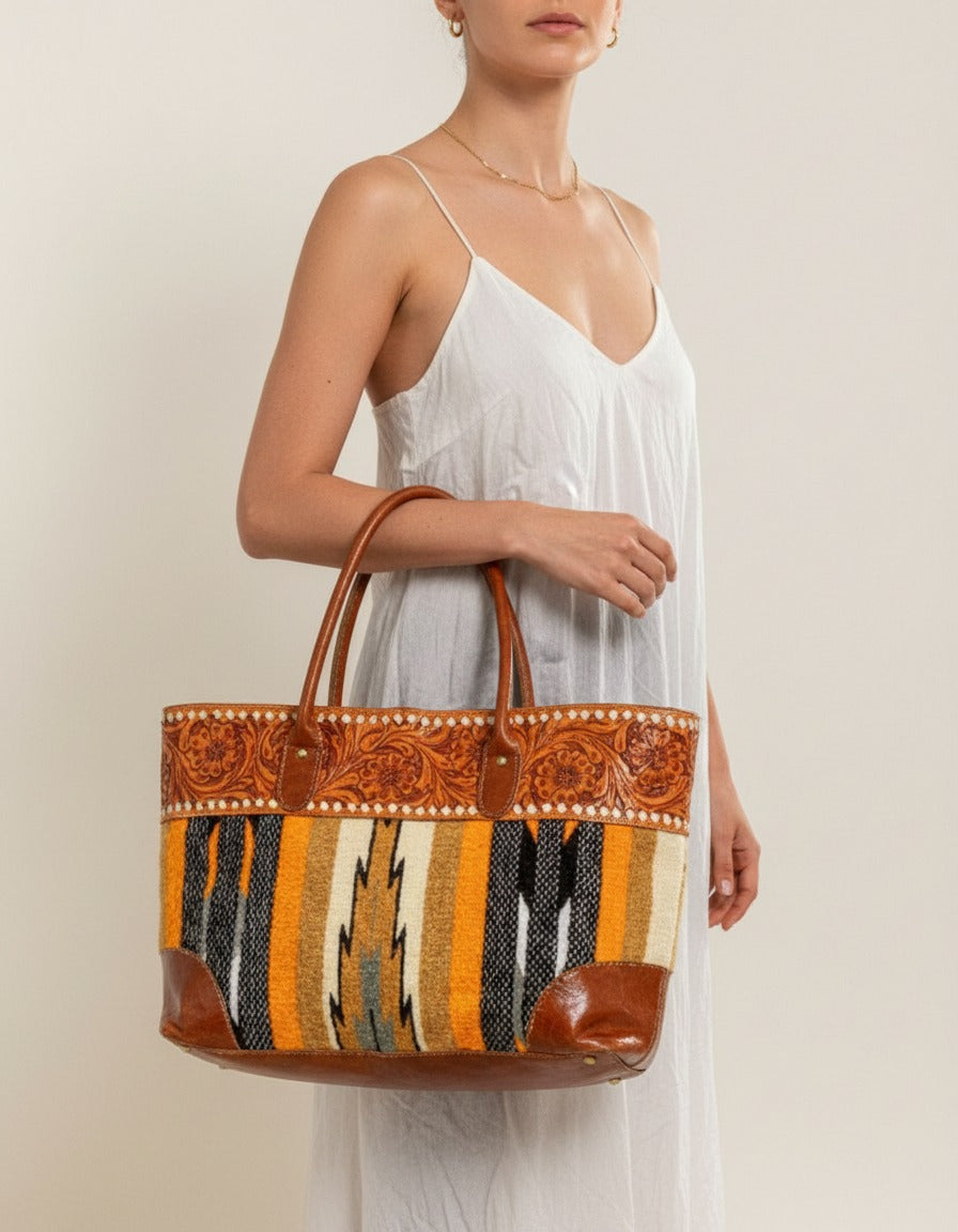 Mustard serape woven zip tote with tooled leather band, worn by a model, by Ya Qalbi