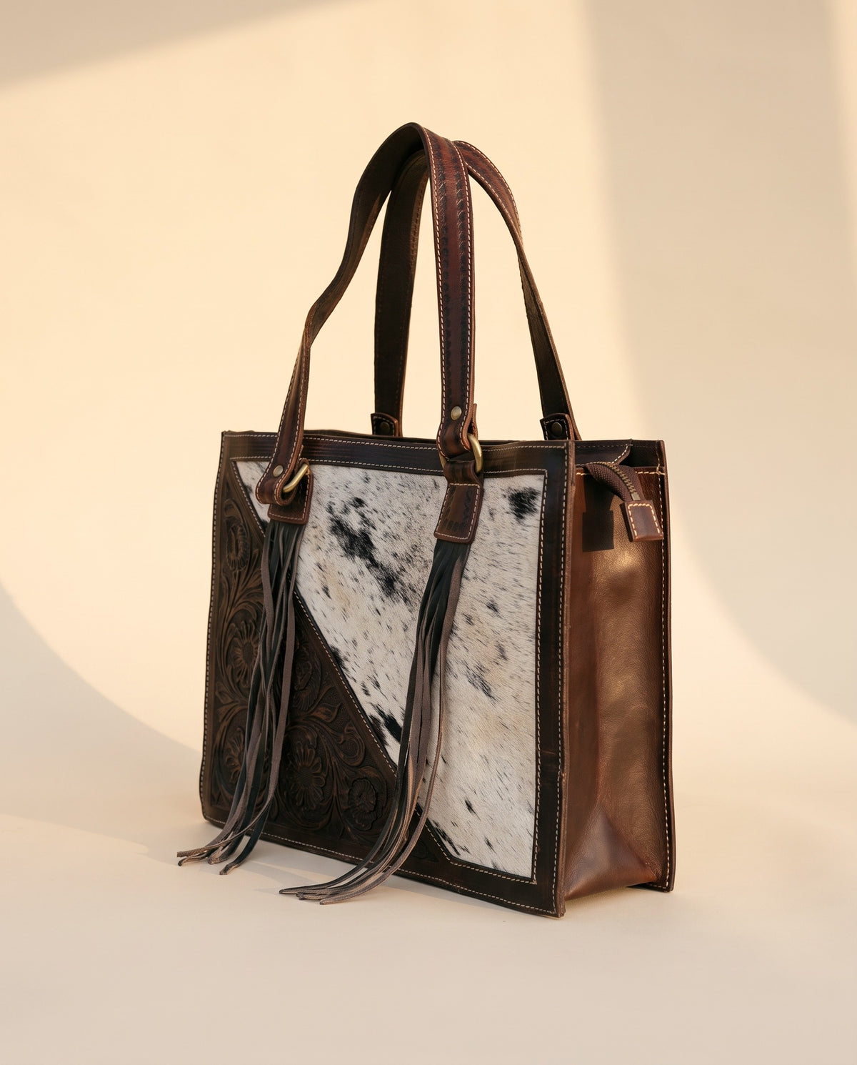 Dark brown tooled triangle hair-on cowhide leather tote with fringe, angled view, by Ya Qalbi