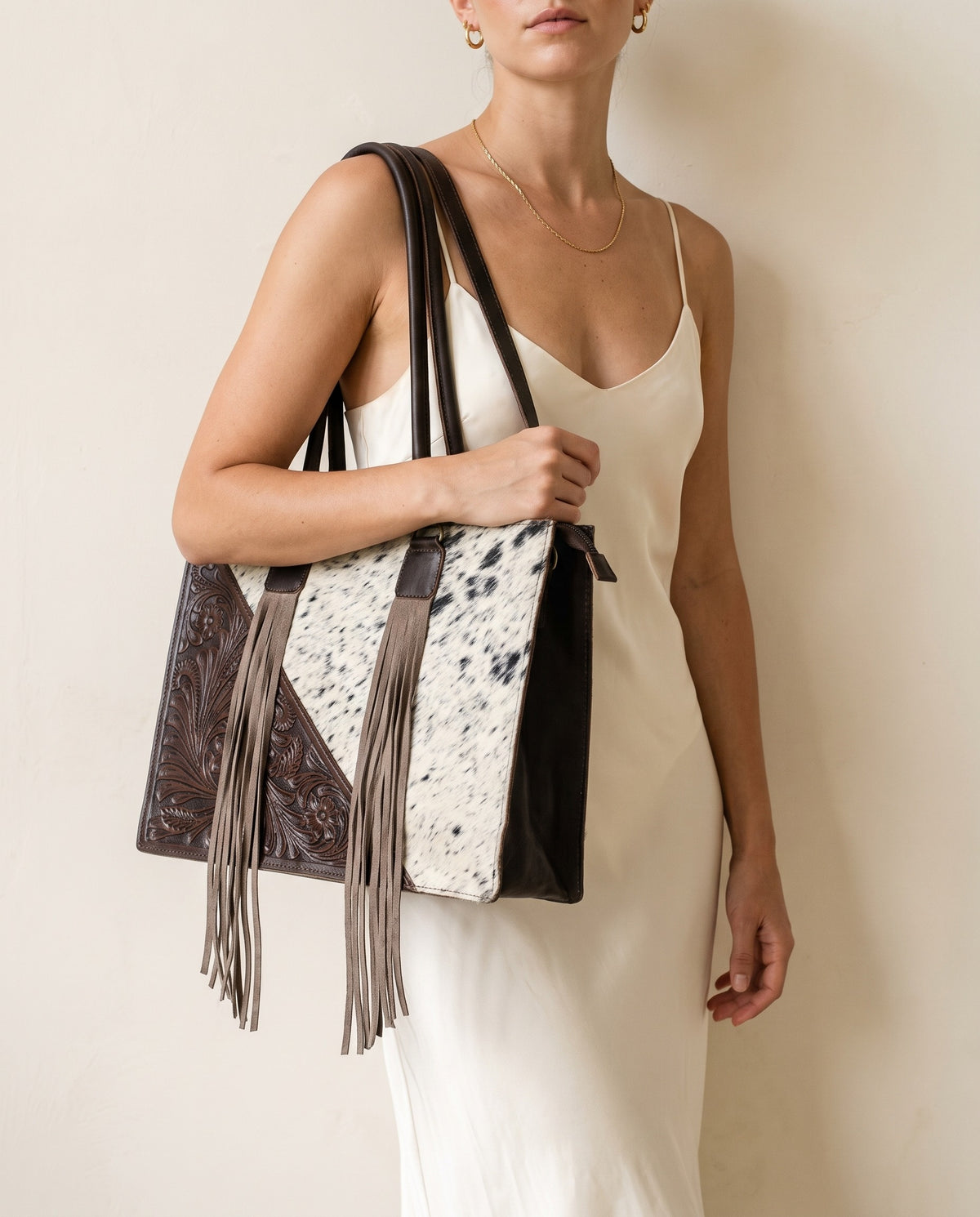 Dark brown tooled triangle hair-on cowhide leather tote with fringe, worn by a model, by Ya Qalbi
