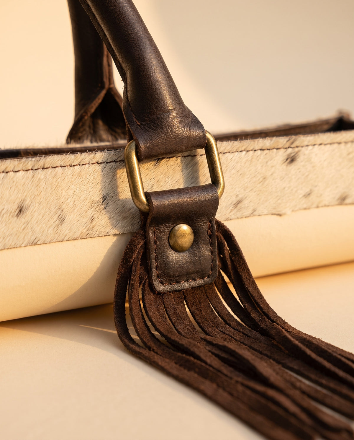 Tan tooled triangle hair-on cowhide leather tote with fringe, buckle-tab handle and fringe close-up, by Ya Qalbi